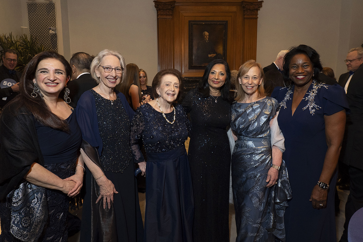 A group of six women wearing blue formal gowns smile at the camera.