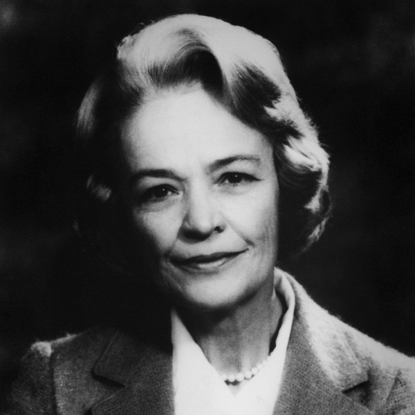 A black and white picture of a woman looking at the camera. She has a slight smile and is wearing a pearl necklace and suit jacket.