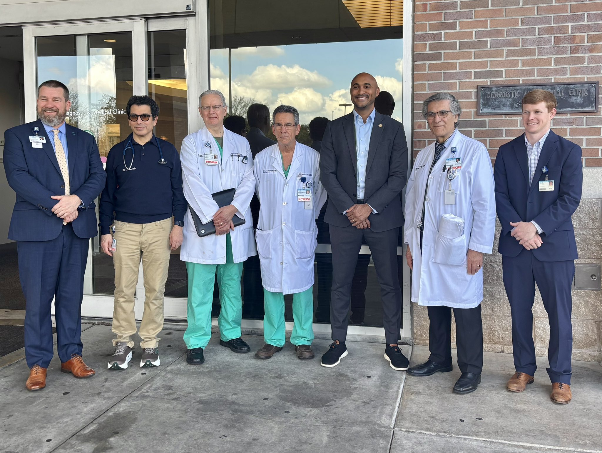 Group of individuals, including several in white clinical coats, standing together outside the entrance of a medical facility during an advocacy visit.